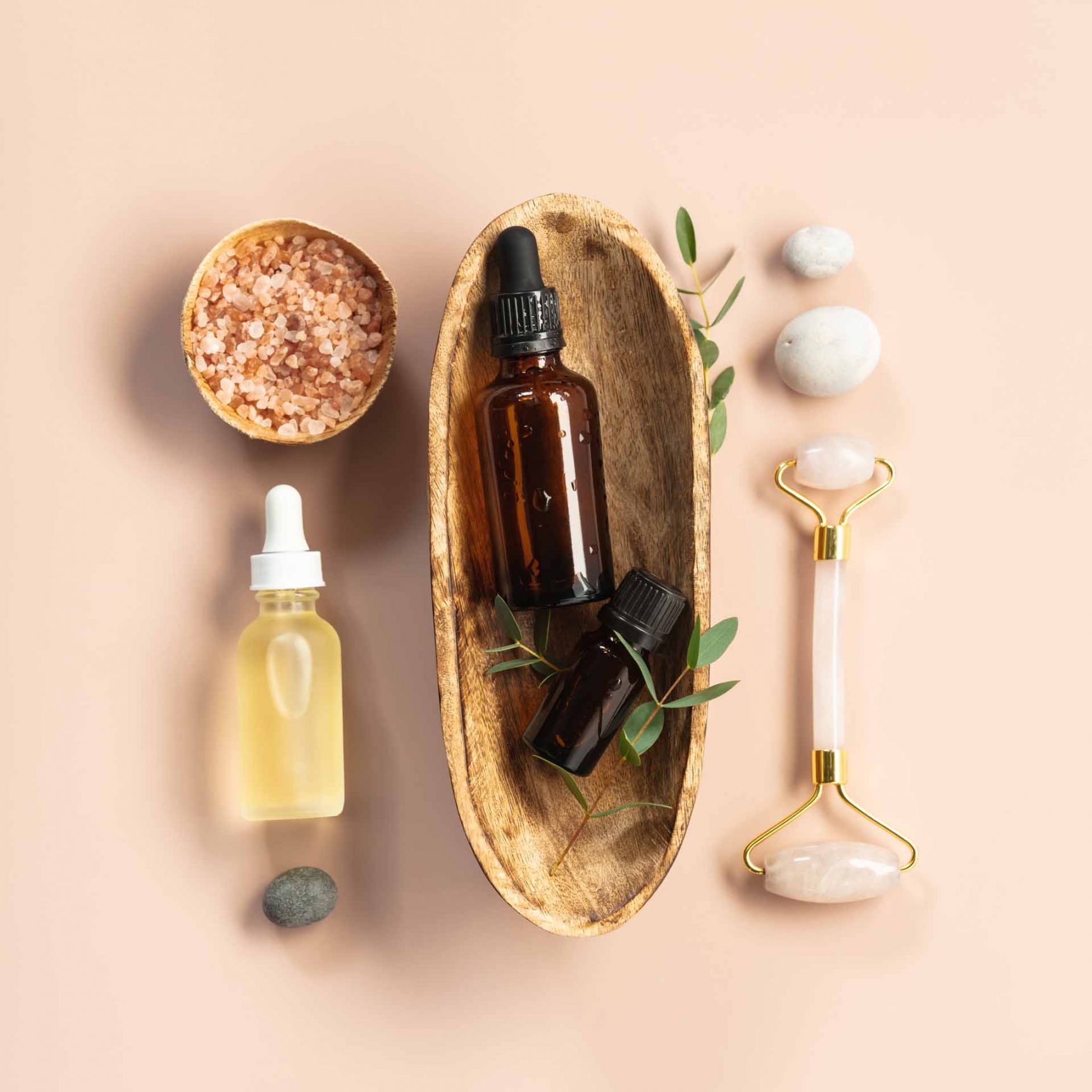 Natural SPA cosmetic products background, Composition with bottles of essential oils, sea salt and massage rollers on pink background, flat lay